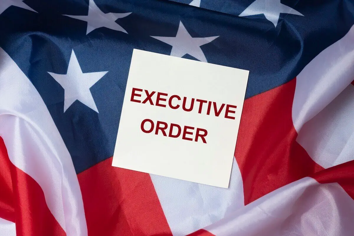 Words 'executive order' written in red on a white notecard lying on a USA flag